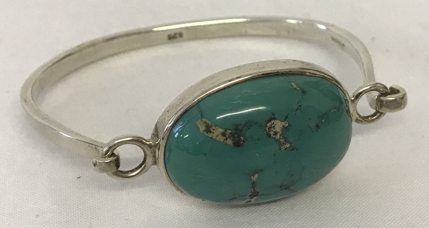 A silver bangle set with a large turquoise stone.