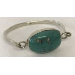 A silver bangle set with a large turquoise stone.