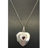 A silver heart shaped locket set with central heart shaped garnet on an 18 inch fine curb chain.