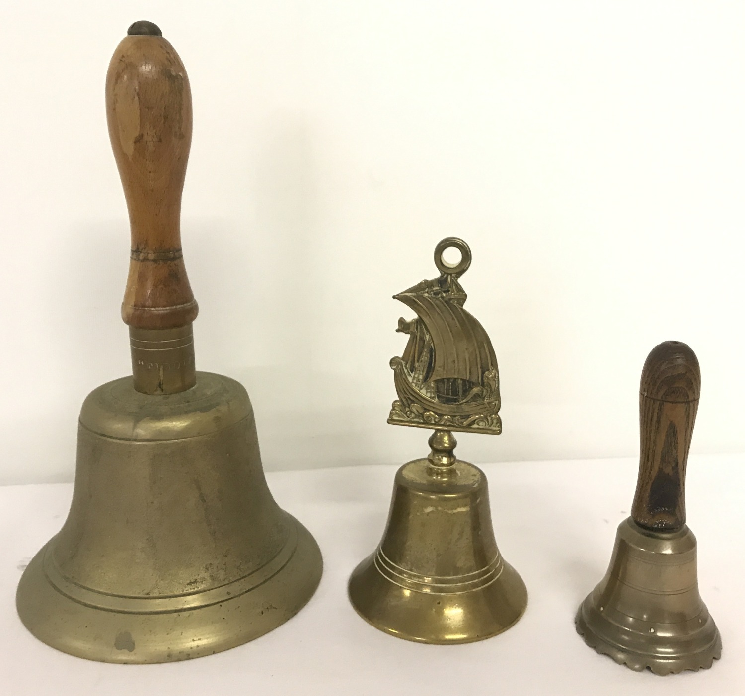 Three brass hand bells of varying sizes, 2 with wooden handles.