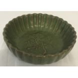A small green glazed ceramic shallow bowl with scalloped edge and blossom detail.