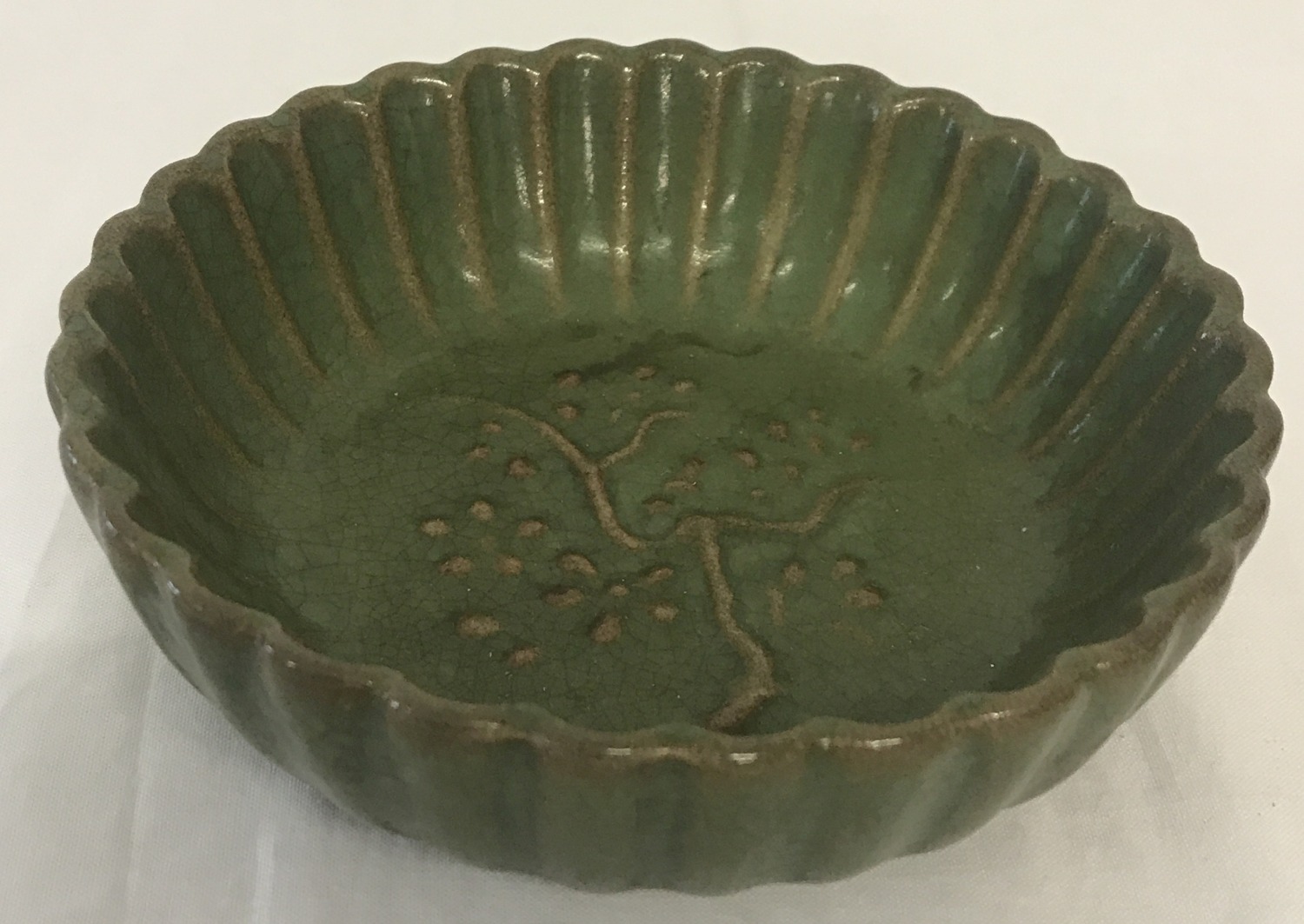 A small green glazed ceramic shallow bowl with scalloped edge and blossom detail.