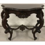 A dark wood decorative hall table with ornately carved legs and stretcher.