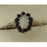 A 9ct gold sapphire and opal dress ring. Central oval cut opal surrounded by 10 small sapphires.