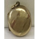 A 9ct gold oval locket with engine turned decoration to front. Approx. 3cm x 1.75cm including bale.