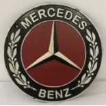 A circular shaped painted cast metal Mercedes Benz wall plaque.