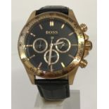 A men's modern chronograph wristwatch by Hugo Boss. Gold tone case with black leather strap.