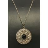 A silver circular decorative locket set with a central onyx stone on an 18" fine curb chain.
