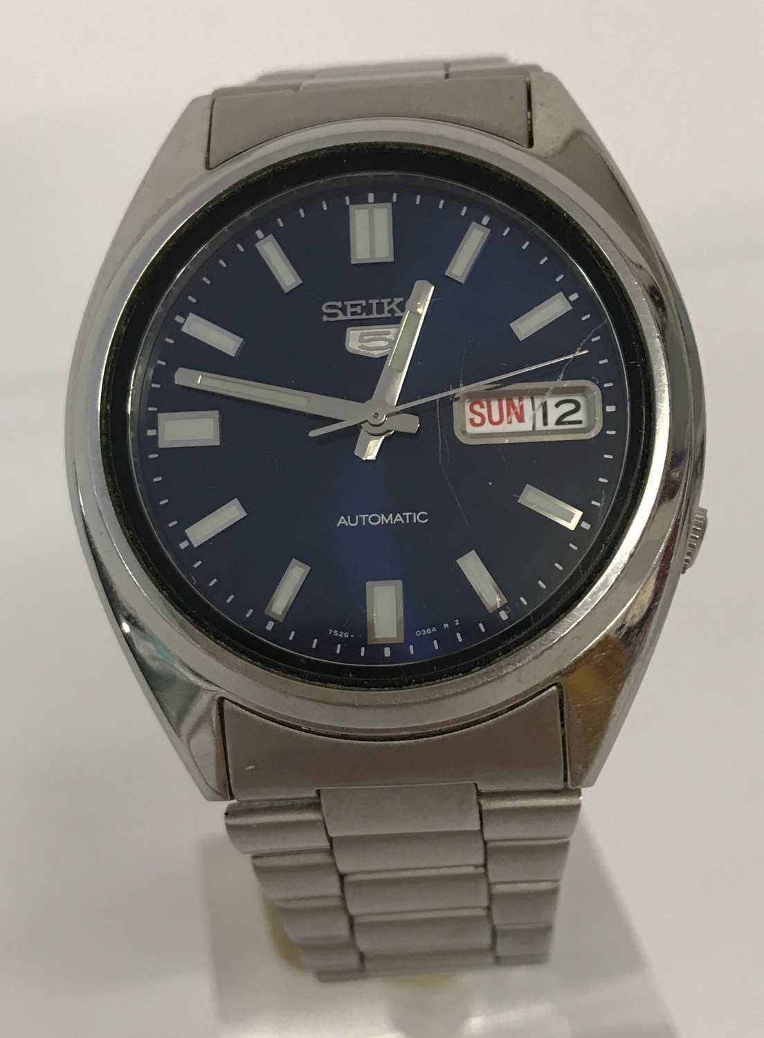 A men's Seiko 5 automatic wristwatch with blue face and see-through back case.