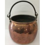 A large antique copper round sided, swing handled cooking cauldron.