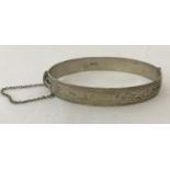 A vintage oval shaped half engraved silver bangle complete with safety chain.