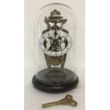 A glass domed Skeleton mantle clock. Brass workings with enamelled face and wooden plinth.