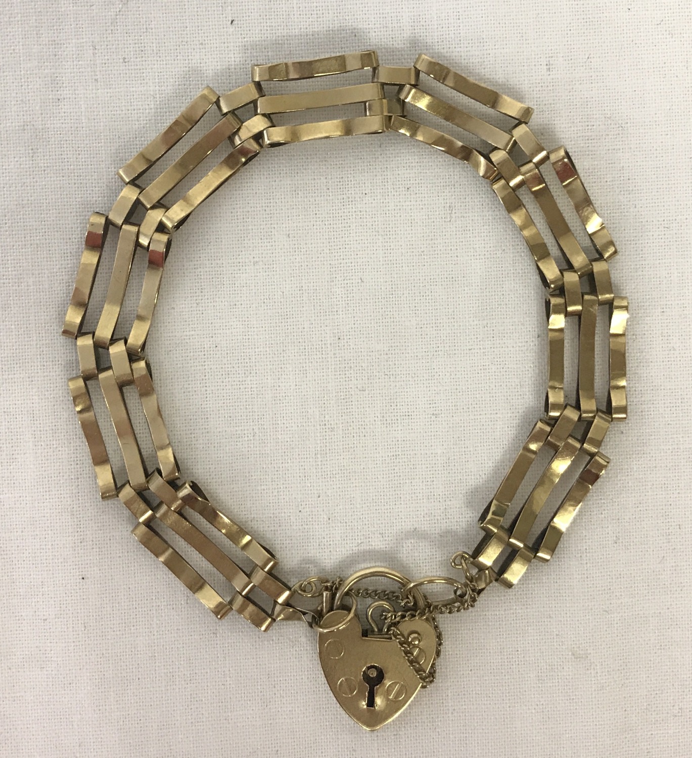 A 9ct gold 3 bar bracelet with padlock and safety chain.