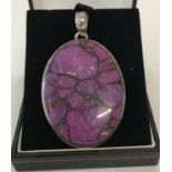 A large oval silver pendant set with purple coloured natural stone.