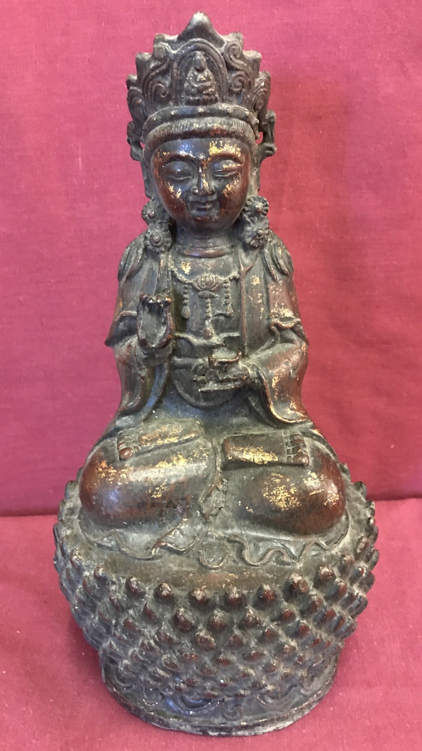 A Chinese hollow bronze figure of a deity sitting upon a lotus flower. With gilt detail.