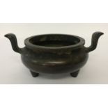 A large Chinese bronze censer with curved upright handles, raised on tripod feet.