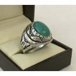 A large white metal dress ring with carved detail and set with oval shaped piece of turquoise.
