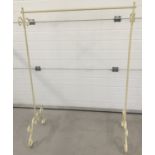 A modern cream painted metal clothes hanging rail with decorative scroll work.