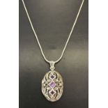 A silver oval locket with pierced work detail to front. Set with square cut amethysts & marcasite's.