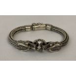 A silver double dragon head bracelet. Two dragon heads holding a silver ring.