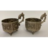 A Pair of Chinese white metal cup holders with dragon shaped handles and raised on tripod feet.