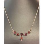 A pendant style silver necklace set with 6 round and oval cabochon garnets.