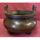 A round Chinese bronze censer with loop handles and tripod feet.