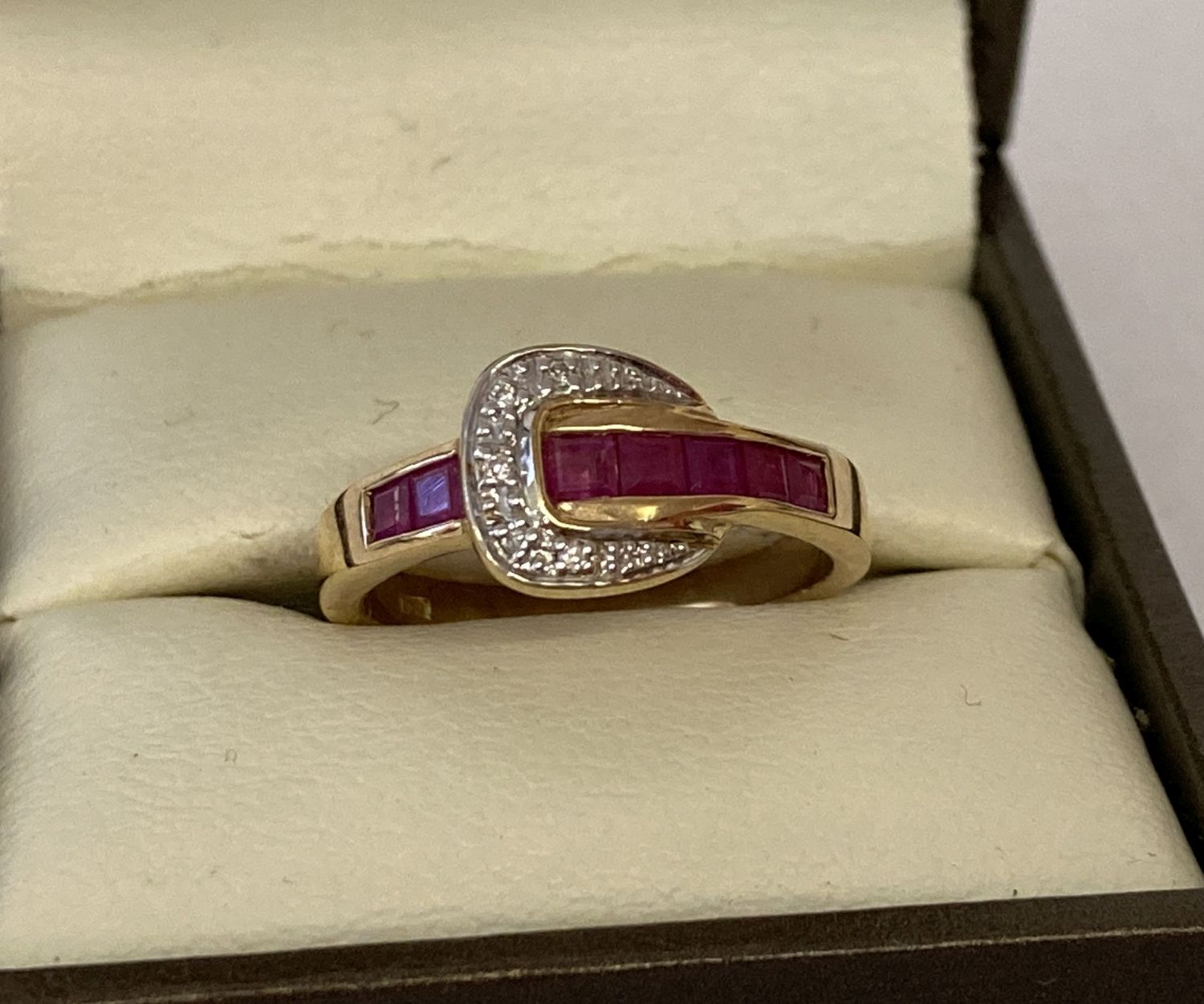 A 9ct gold ruby and diamond set buckle design dress ring, possibly Luke Stockley, London.