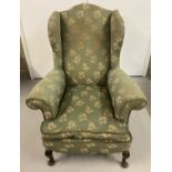 A vintage wing back chair with green & gold upholstery and wooden cabriole feet.