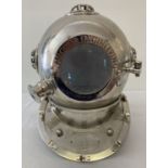 A large ornamental chrome coloured divers helmet with front opening hinged door and glass panels.