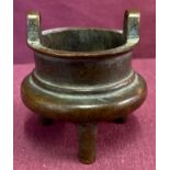 A miniature Chinese bronze censer with loop handles, raised on tripod feet.