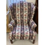 A vintage wooden framed wing back armchair with floral and maroon striped upholstery.