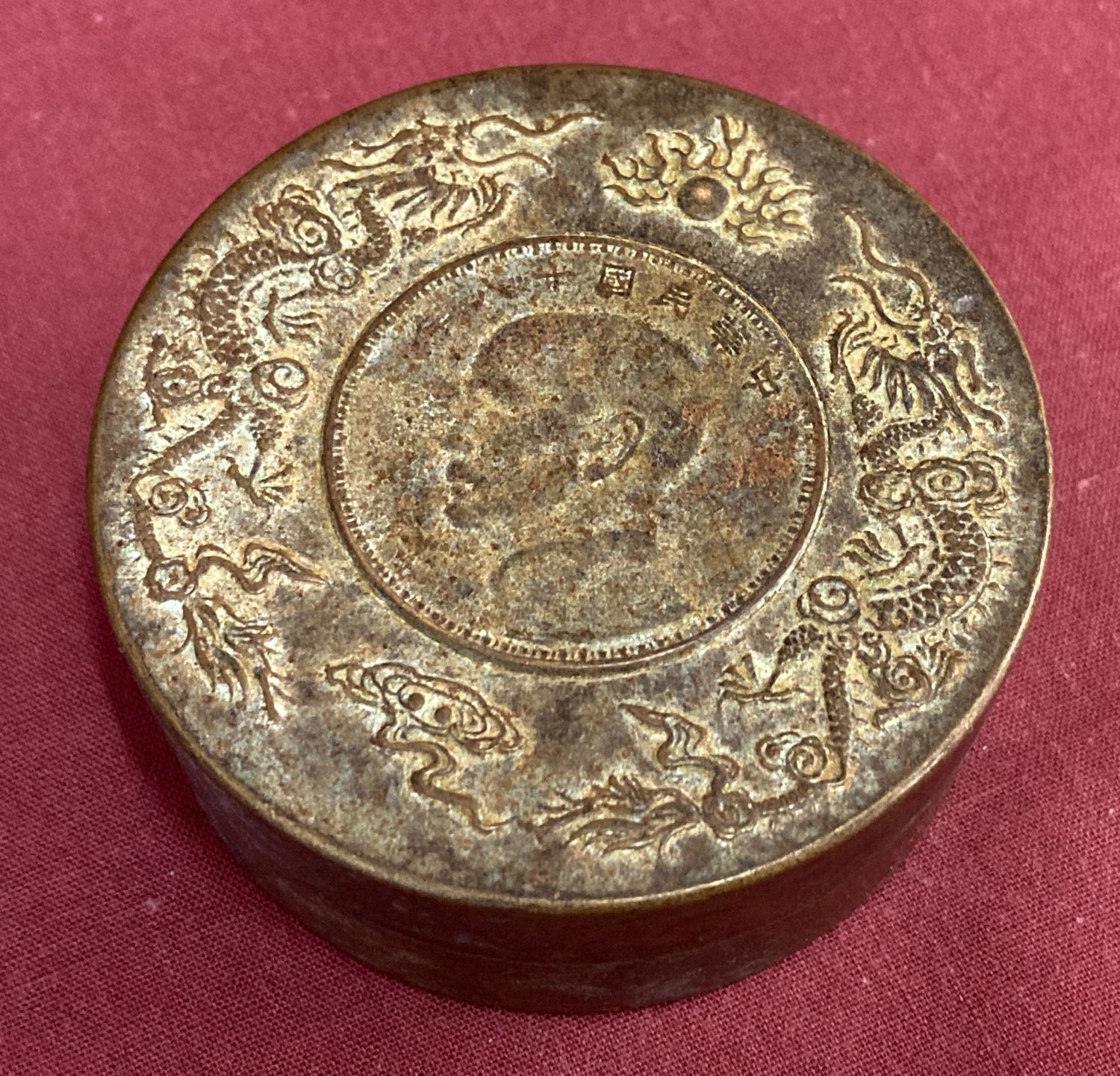 A circular bronze scroll weight with dragon detail to top rim.