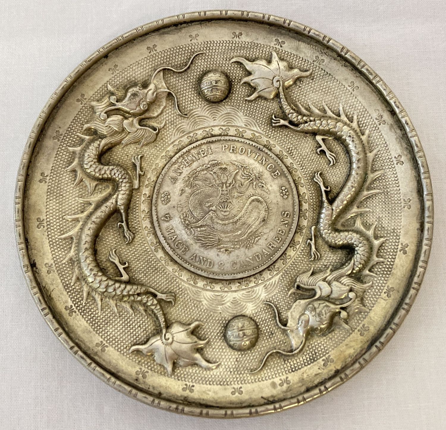 A Chinese white metal coin dish, made from central coin with white metal surround featuring dragons.