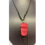 A carved coral pendant in the shape of a Chinese Nuo mask on a woven string expandable necklace.