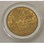A gold coloured Chinese coin in a clear plastic case.