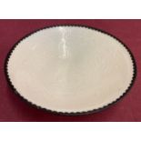 A small white glazed dish with scalloped metal rim.