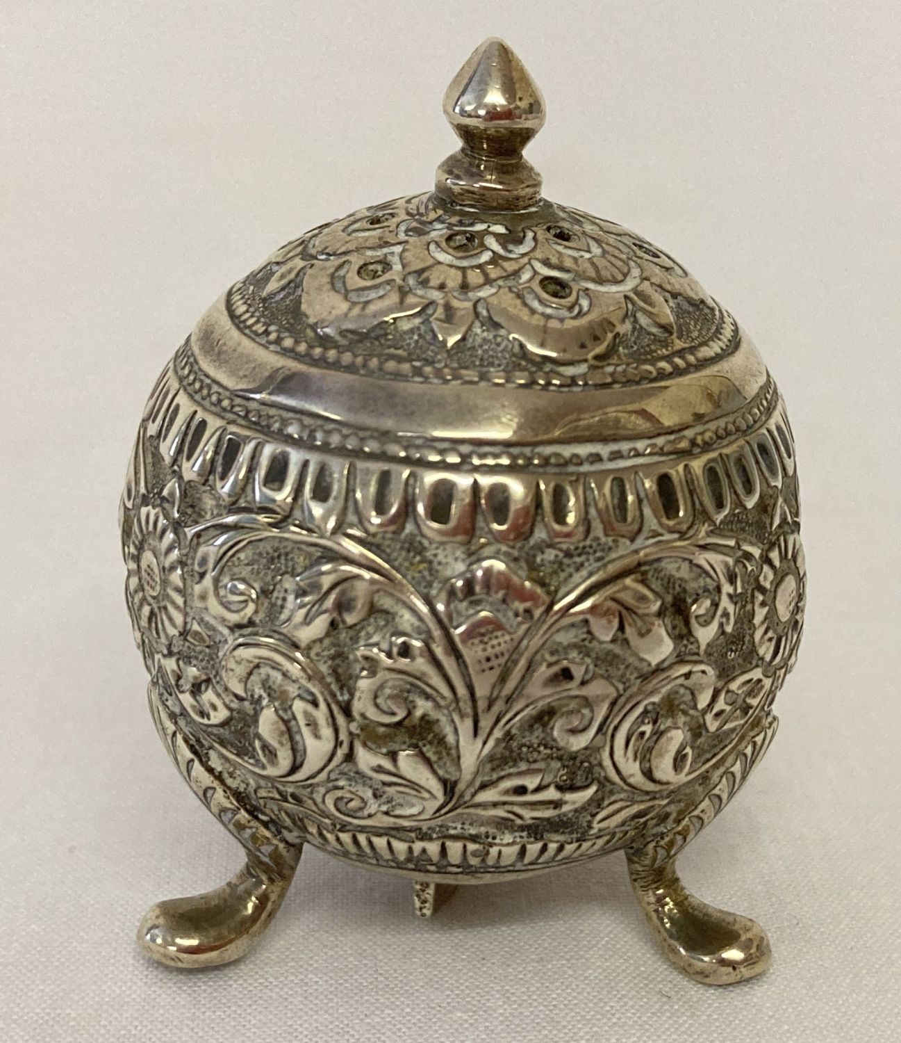 A Persian silver 3 footed pepperette of spherical form, with ornate floral decoration throughout.