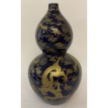 A large ceramic, bottle gourd shaped vase. Deep blue glaze with gilt dragon and symbol detail.