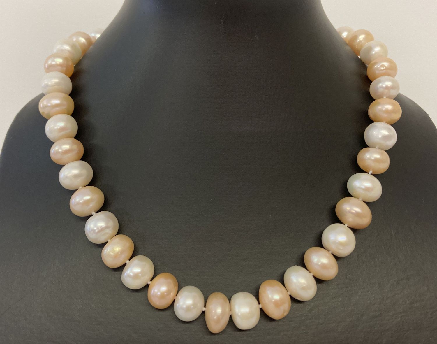 A 16" string of larger oval shaped alternate cream & peach freshwater pearls, with magnetic clasp.