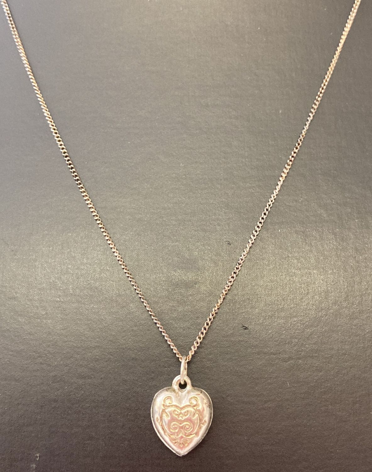 A decorative silver heart shaped pendant on an 18" fine curb chain.