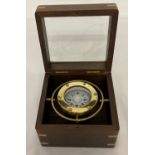 A modern small brass ships compass in a glass topped wooden box.