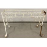 A white painted wrought iron plant stand with scroll detail and legs.