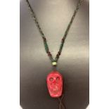 A carved coral pendant in the shape of a skull, on a woven string expandable necklace.