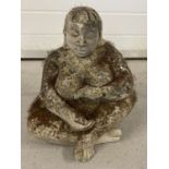 A carved concrete garden ornament "Mother Earth" of a seated naked woman.