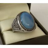 A men's silver dress ring set with a pale blue cabochon stone. Greek key detail to both shoulders.