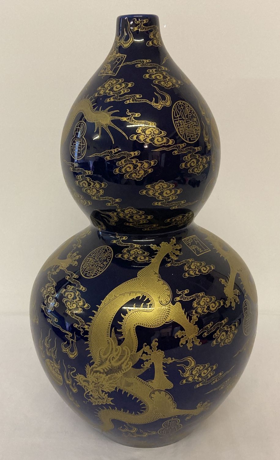 A large ceramic, bottle gourd shaped vase. Deep blue glaze with gilt dragon and symbol detail.