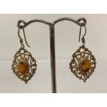 A pair of silver filigree design drop earrings each set with an oval amber stone.
