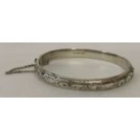 A vintage silver hinged bangle with half floral engraved decoration and safety chain.