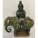 A stoneware ceramic elephant figurine carrying a gourd, in blue/green majolica style glaze.